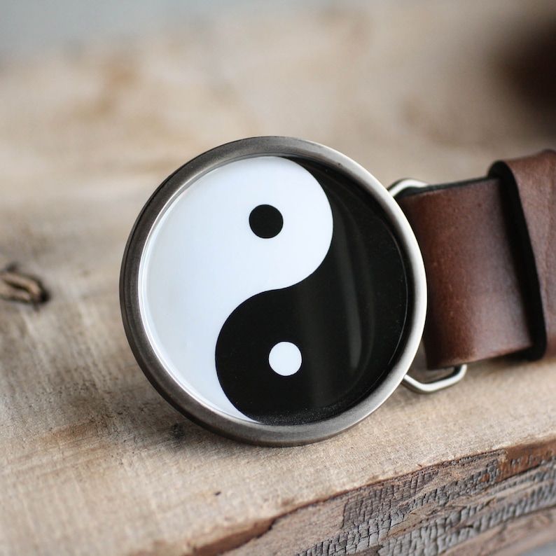May include: A silver belt buckle with a black and white yin yang symbol.