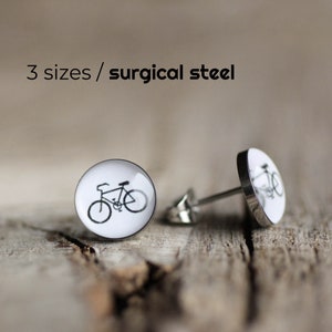 Może przedstawiać: Para srebrnych kolczyków z białym tłem i czarnym wzorem roweru. Kolczyki wykonane są ze stali chirurgicznej. 3 rozmiary / stal chirurgiczna.