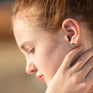 May include: A young person with red hair wearing a small, round, iridescent blue gemstone earring.