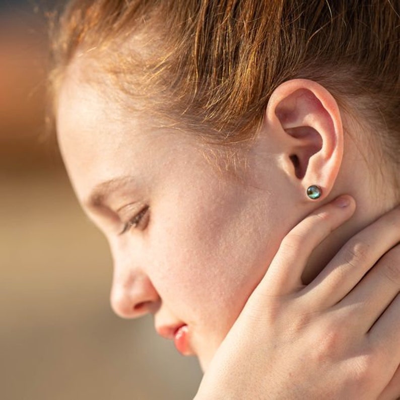 May include: A young person with red hair wearing a small, round, iridescent blue gemstone earring.