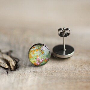 May include: A pair of silver stud earrings with a round, colorful floral design. The earrings have a post and butterfly back.