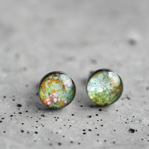 May include: A pair of silver stud earrings with a floral design. The earrings feature a round, clear glass cabochon with a colorful floral pattern.