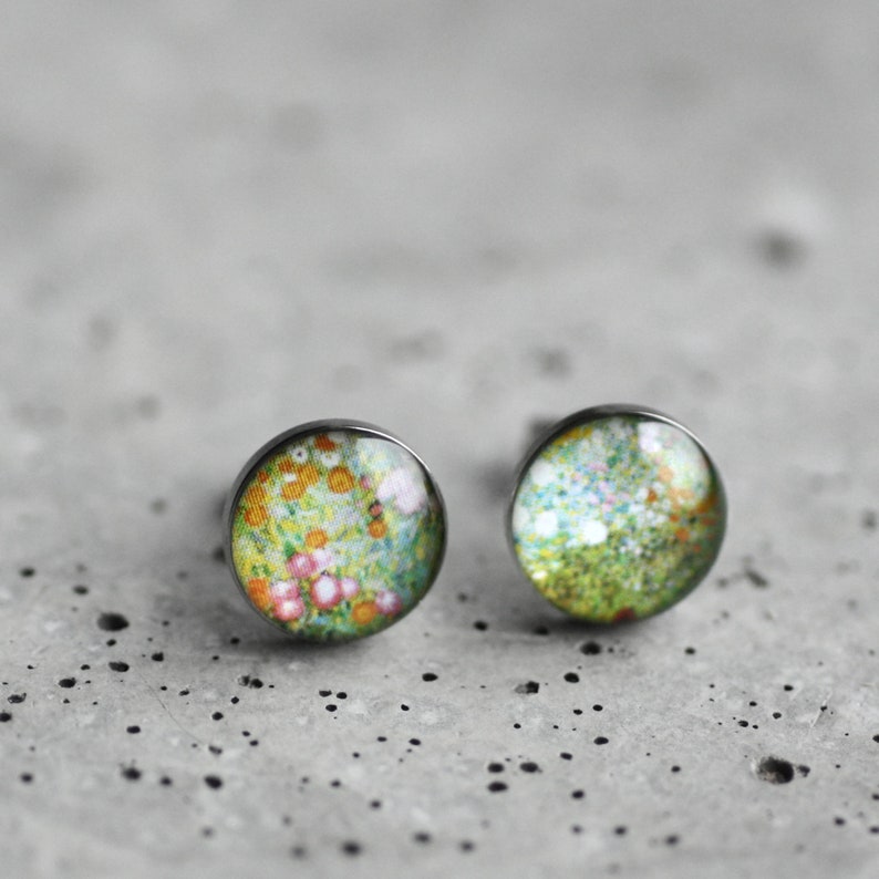 May include: A pair of silver stud earrings with a floral design. The earrings feature a round, clear glass cabochon with a colorful floral pattern.