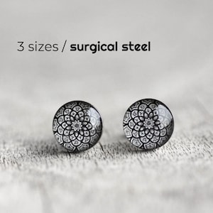 Può includere: Un paio di orecchini a lobo rotondi con un motivo mandala in bianco e nero. Il testo 3 sizes / surgical steel è stampato sopra gli orecchini. Gli orecchini presentano una finitura liscia e lucida e una forma circolare con dettagli floreali.