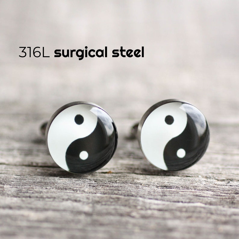 May include: A pair of silver cufflinks with a black and white yin yang symbol design. The cufflinks are made of 316L surgical steel.