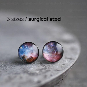 May include: A pair of surgical steel stud earrings with a galaxy print. The earrings are round and have a silver backing.