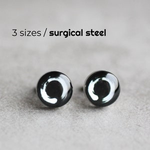 May include: A pair of silver stud earrings with a black and white circle design. The earrings are made of surgical steel.