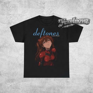 May include: Black t-shirt featuring the band name "deftones" in light blue script above an anime-style illustration of a woman in a red suit. The text "around the fur" is below the band name.