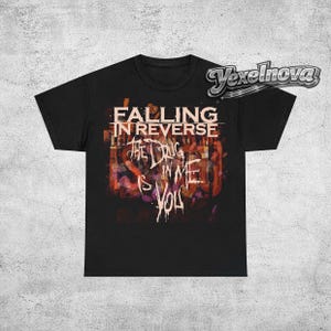 May include: Black t-shirt featuring the band name "Falling in Reverse" in a stylized font above the text "The Drug is in Me, You". The graphic has a colorful, abstract background.