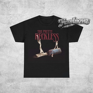 May include: Black t-shirt featuring the text "THE PRETTY RECKLESS" in burgundy. The graphic includes an illustration of a wrapped object with smoke rising from it. The shirt is a classic crew neck style.