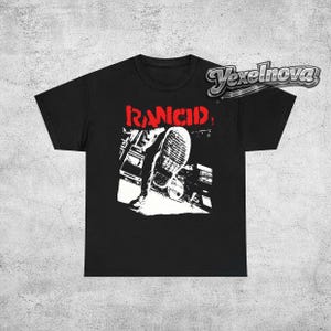 Puede incluir: Camiseta negra con la palabra "RANCID" en rojo sobre un gráfico en blanco y negro de un pie pisando una superficie. La camiseta tiene cuello redondo y mangas cortas.