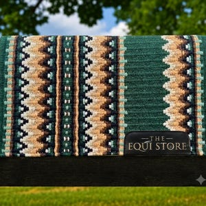 Op de afbeelding: Een rechthoekig zadeldek met een getextureerd groen oppervlak en een verticaal patroon van zigzagstrepen in tinten beige, donkerbruin, wit en lichtblauw. Een zwarte leren patch in de hoek bevat de tekst THE EQUI STORE.