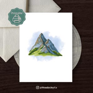 Op de afbeelding: Een aquarelprint van twee bergtoppen in blauwe en bruine tinten, tegen een lichtblauwe achtergrond. Groen gras accentueert de basis van de bergen. De print is gelabeld met "Printable" met een printerpictogram.