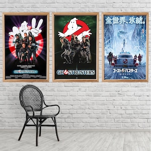 Puede incluir: Tres carteles de películas enmarcados con temas de Los Cazafantasmas. Los carteles incluyen el logotipo y los personajes de Los Cazafantasmas. Un cartel está en japonés. Los carteles se exhiben en una pared de ladrillos blancos.