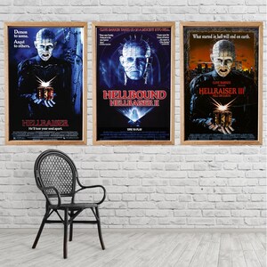Könnte beinhalten: Drei gerahmte Filmplakate aus der Hellraiser-Filmreihe. Die Poster zeigen dunkle Hintergründe mit Bildern der Figur Pinhead und Filmtiteln. Vor einer weißen Backsteinmauer steht ein schwarzer Korbstuhl.