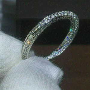 May include: A silver-toned eternity band ring featuring a continuous row of small, clear, round-cut stones set along the entire outer circumference of the metal band, creating a highly reflective and sparkling appearance across the surface.