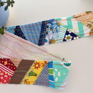 Peut inclure: Deux bandes de tissu patchwork colorées avec des bords en zigzag. Les bandes présentent divers motifs, notamment floraux, géométriques et abstraits, dans des tons de rouge, jaune, bleu et marron. Les bandes font probablement partie d'un projet artisanal plus vaste.