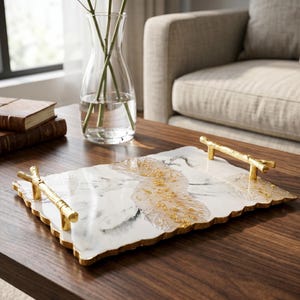 May include: A rectangular serving tray featuring a white and gray faux marble surface with a central translucent resin inlay embedded with gold flakes. The tray includes two gold-colored metal handles shaped like textured tree branches.