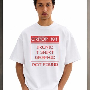 Op de afbeelding: Een wit T-shirt met korte mouwen en een rode, gepixelde afbeelding op de borst. De tekst luidt ERROR 404: IRONIC T SHIRT GRAPHIC NOT FOUND, omsloten door een rechthoekige rand. Het ontwerp heeft een versleten, verweerde textuur.