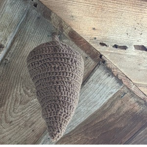 Puede incluir: Un cono de crochet marr&oacute;n colgando de un techo de madera. El cono est&aacute; hecho de un hilo grueso y tiene una punta puntiaguda.