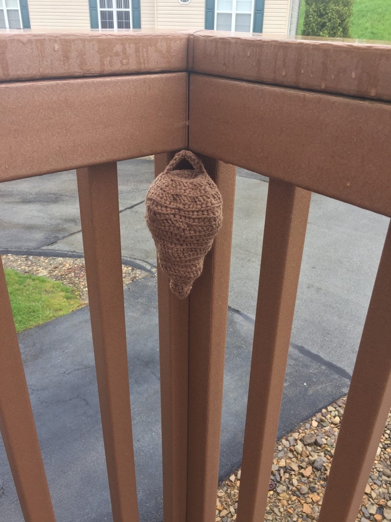 Puede incluir: Un macetero colgante de ganchillo marr&oacute;n est&aacute; sujeto a una barandilla de madera marr&oacute;n.