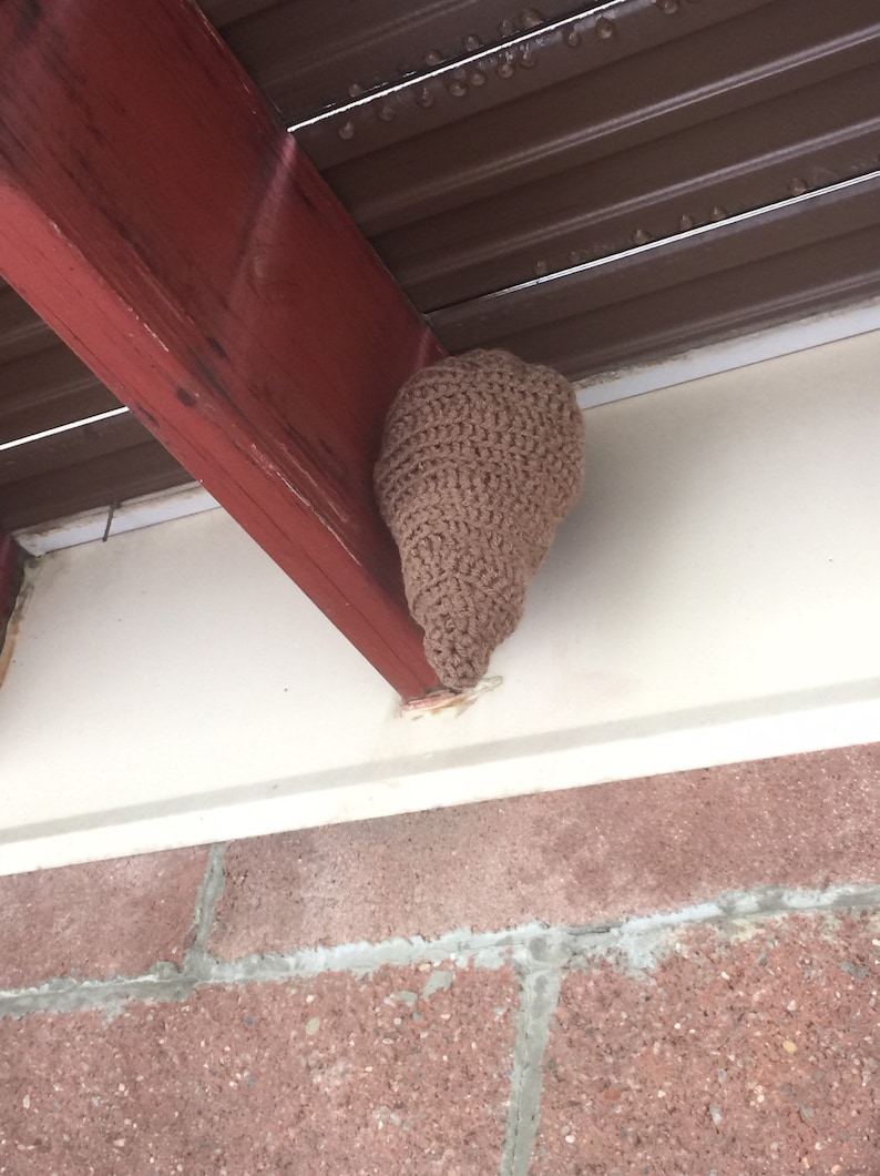 Puede incluir: Una colmena de crochet marr&oacute;n colgada de una viga de madera bajo un toldo de metal marr&oacute;n.