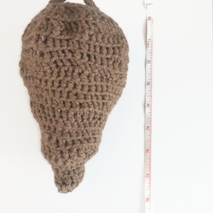 Puede incluir: Una cesta colgante de crochet de forma de l&aacute;grima de color marr&oacute;n con un bucle en la parte superior. La cesta mide aproximadamente 18 cm de alto.