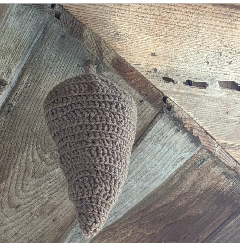 Puede incluir: Un cono de crochet marr&oacute;n colgando de un techo de madera. El cono est&aacute; hecho de un hilo grueso y tiene una punta puntiaguda.