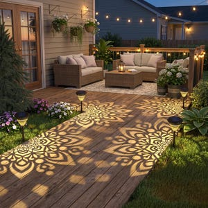 May include: A set of solar-powered garden path lights with black stakes and textured tops that cast intricate, glowing mandala-like patterns onto a wooden deck. The lights are positioned along the edge of a lawn, illuminating the walkway.