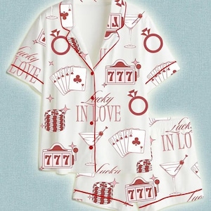 Könnte beinhalten: Weißes Pyjama-Set mit Casino-Motiv. Das kurzärmelige Oberteil und die Shorts haben rote Akzente und Illustrationen von Spielkarten, Martinigläsern, Spielautomaten und dem Text "Lucky in Love."