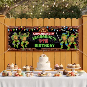 Può includere: Uno striscione rettangolare in vinile con i personaggi delle Tartarughe Ninja, una grafica di pizza e il testo Cowabunga! Leonardo's 9th Birthday. Lo striscione è appeso a una staccionata in legno sopra un tavolo con una torta e cupcake.