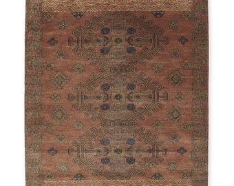 May include: A rectangular, terracotta-colored rug with an intricate geometric pattern. The central design features repeating shapes in navy blue, olive green, and gold. The border has a lighter tan hue with floral and geometric motifs.