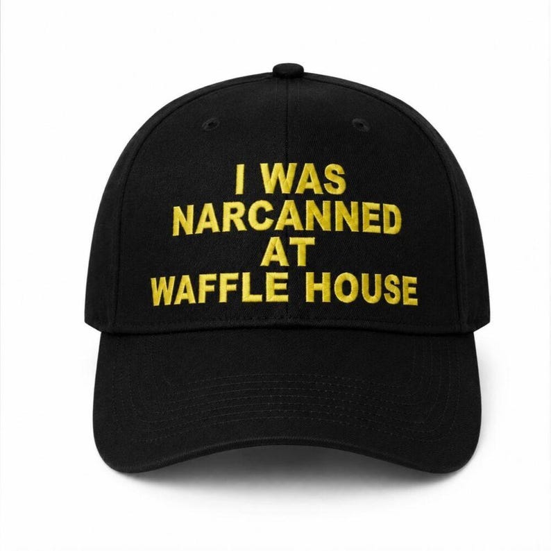 May include: Black baseball cap with the embroidered text "I WAS NARCANNED AT WAFFLE HOUSE" in yellow. The cap has a curved brim and a structured crown, suitable for casual wear.