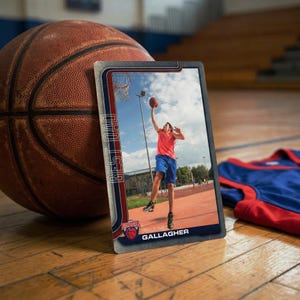 May include: A basketball card with a photo of a person shooting a basketball, labeled "Best Dad" and "Gallagher." A basketball and a blue and red jersey are also in the image.