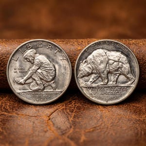 May include: Two silver half-dollar coins. One coin features a miner panning for gold with the inscription "LIBERTY" and "CALIFORNIAS-DIAMOND JUBILEE 1925". The other coin shows a bear and reads "UNITED STATES OF AMERICA HALF DOLLAR".