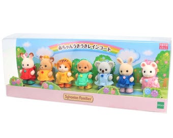May include: A Sylvanian Families toy set featuring seven miniature animal figures wearing colorful raincoats in red, yellow, orange, green, light blue, dark blue, and pink, all packaged in a clear rectangular box with a rainbow graphic.