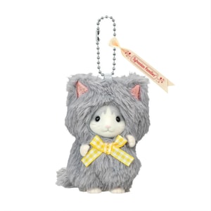 May include: A plush cat keychain featuring a grey furry hood with pink-lined ears, a white face, and a yellow and white gingham bow. A silver ball chain is attached to the top, along with a cream-colored ribbon printed with Sylvanian Families.