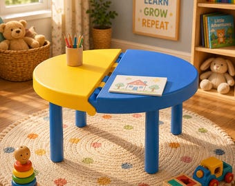 Puede incluir: Una mesa infantil semicircular de dos tonos con patas azules. La parte superior de la mesa está dividida en secciones amarillas y azules. Un pequeño dibujo de una casa se encuentra en el lado azul. La alfombra debajo de la mesa es beige con lunares coloridos. Un tren de juguete de madera y un juguete apilable están cerca.
