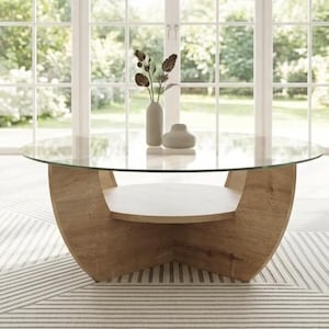 Könnte beinhalten: Ein runder Couchtisch mit einer transparenten Glasplatte und einem hellbraunen Holzsockel. Der Sockel hat ein einzigartiges geschwungenes Design mit einem unteren Regal. Zwei kleine, neutralfarbene Vasen mit dekorativen Stielen stehen auf dem Tisch.