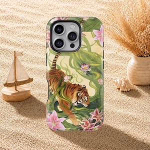 Peut inclure: Une coque de téléphone avec une illustration à l'aquarelle d'un tigre au milieu d'un feuillage vert et de lys roses. Le tigre a des rayures orange et noires. La coque a un bord noir et une découpe pour l'appareil photo.