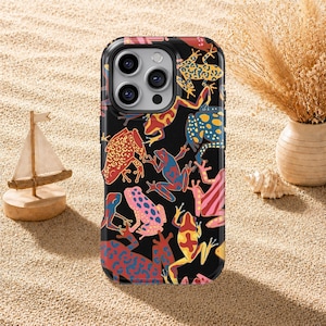 Puede incluir: Una funda de smartphone negra con un patrón vibrante y repetitivo de varias ranas coloridas en tonos amarillos, azules, rojos y rosas. El diseño cubre toda la parte posterior de la funda, incluyendo el área alrededor de la triple lente de cámara.