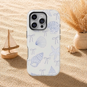 Puede incluir: Una funda para smartphone de color blanco con un patrón repetitivo de ilustraciones de líneas azules que representan diversas conchas marinas, estrellas de mar y pequeños lazos. La funda tiene un recorte negro para la cámara.