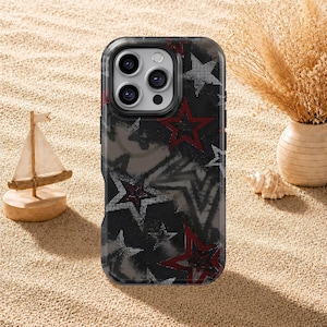 Puede incluir: Una funda para smartphone con un fondo oscuro y texturizado que presenta un patrón de estrellas superpuestas en tonos rojo, blanco y gris. La funda tiene un recorte rectangular para un sistema de triple cámara en la parte posterior.