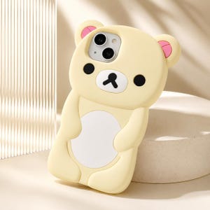 Può includere: Una custodia per telefono in silicone giallo pallido a forma di orso con orecchie arrotondate e accenti rosa. Il viso presenta occhi circolari neri, naso e bocca neri su una toppa bianca. Un grande ovale bianco è centrato sul busto dell'orso.