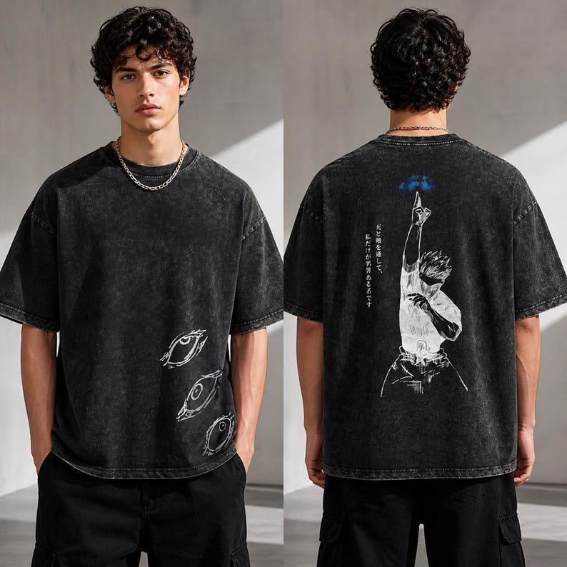 May include: Black acid wash t-shirt with white graphic designs. The front features three stylized eye illustrations. The back displays a figure reaching upwards with Japanese text. The shirt has a relaxed fit and short sleeves.