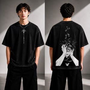 May include: Black oversized t-shirt with a distressed wash. The front features a white graphic and Japanese text. The back displays a detailed black and white illustration of a character with hands on their head. The model is wearing black cargo pants.