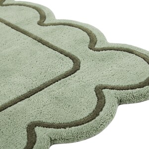 May include: A sage green bath mat with a soft, plush texture and a scalloped edge design. The mat features a darker olive green piped border that follows the curved, wavy outline of the rug, creating a distinct decorative frame around the center.