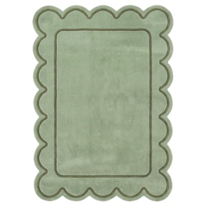 May include: A rectangular sage green rug featuring a scalloped edge design. The rug has a soft, plush texture with a darker green border that follows the scalloped perimeter, creating a distinct frame around the solid, light green center area.