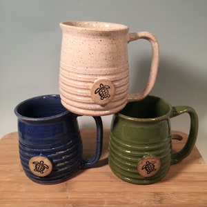 May include: Three ceramic mugs with a speckled glaze and a raised turtle design. The mugs are in white, blue, and green.