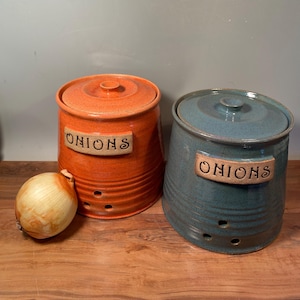 May include: Two ceramic onion storage containers with lids. One is orange and the other is blue-green. Both have the word "ONIONS" written on them.